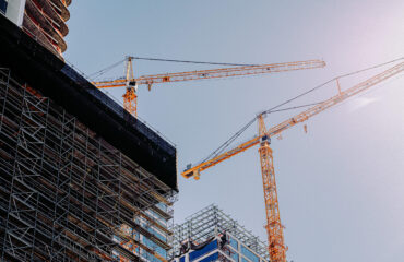 Low angle of two cranes in a construction site under a clear sky background UAE Construction Costs